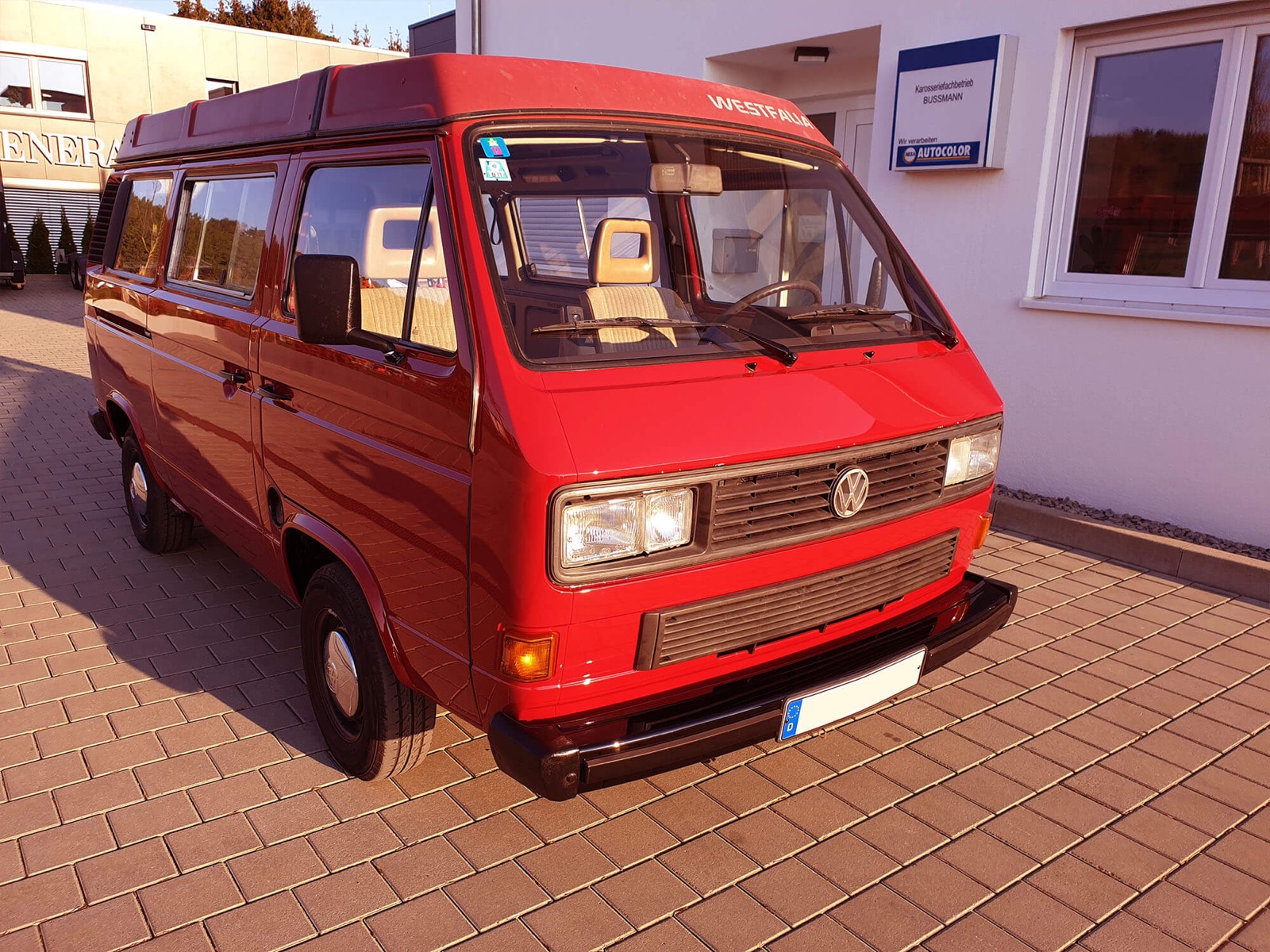 Ein roter VW-Bus T3 steht vor dem Eingang des Karosseriefachbetriebs Bussmann.