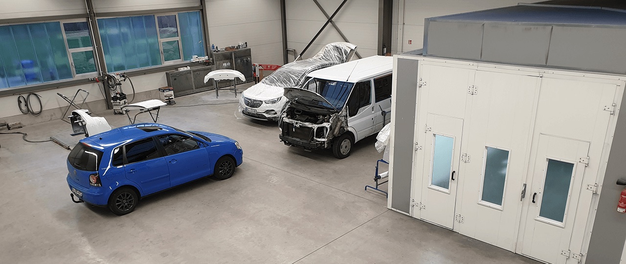 Blick in die Werkstatthalle: ein blauer VW Polo, ein Transporter mit geöffneter Front und die Lackierkabine.