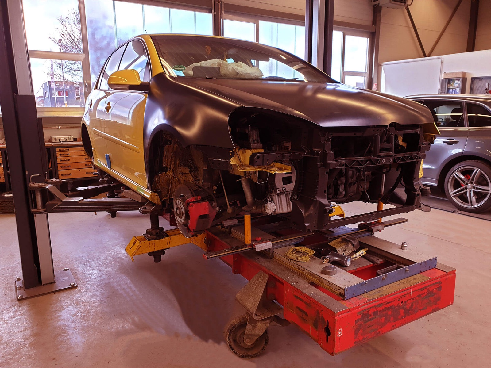 Ein gelber VW Golf mit neuem, grundiertem Kotflügel steht auf der Richtbank in der Werkstatt.